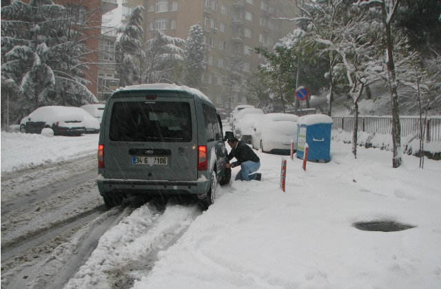 A man putting chain on a tire of his car to be able drive in snow.